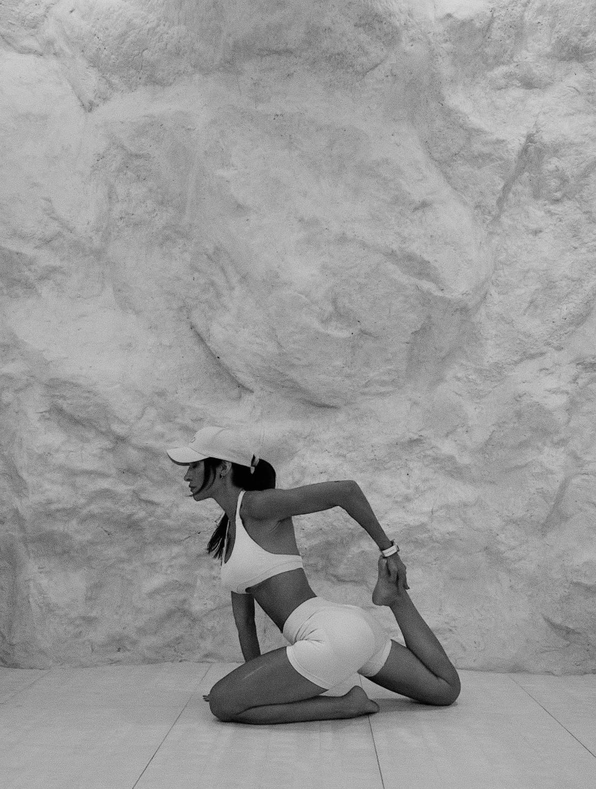 Black-and-white photograph of Demy in a kneeling stretch against the sculpted studio wall