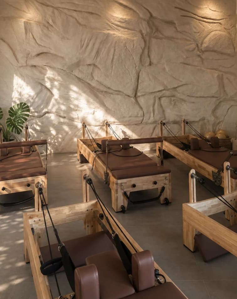 The cave-like CÉLINE studio interior with wooden reformers and sunlight on the sculpted stone wall