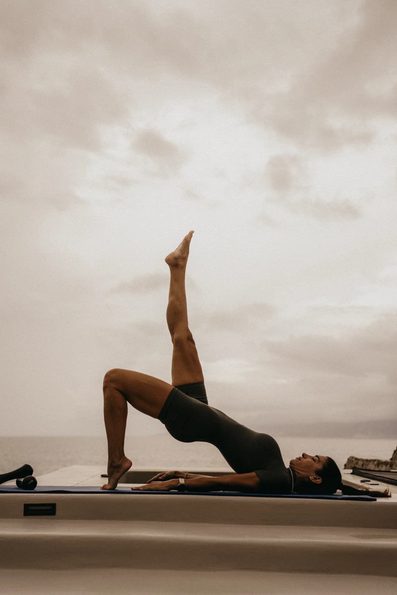 Outdoor reformer session against an open sky — a single leg lifted in a long line